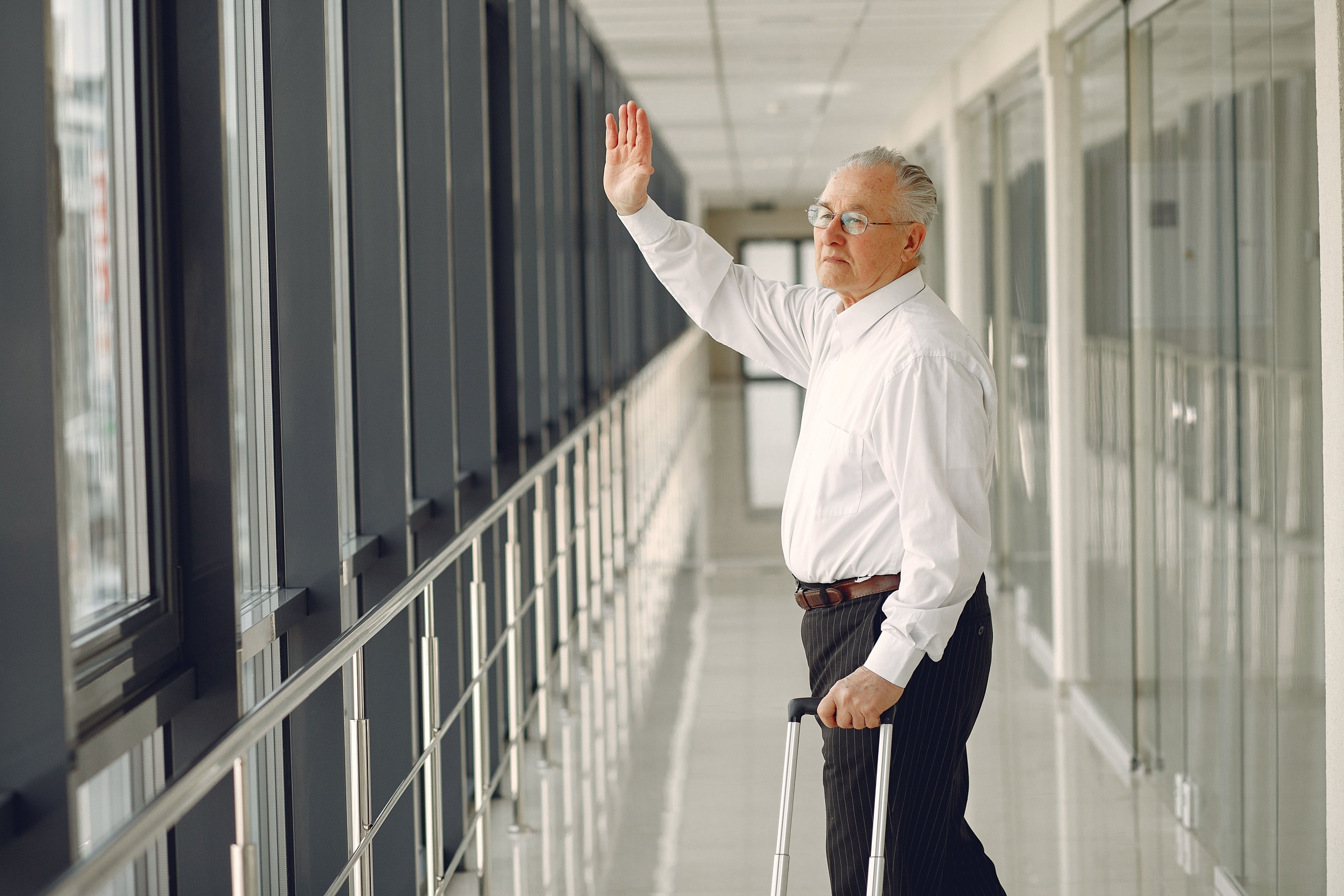 An older man with a suitcase waving as he walks along an airport corridor