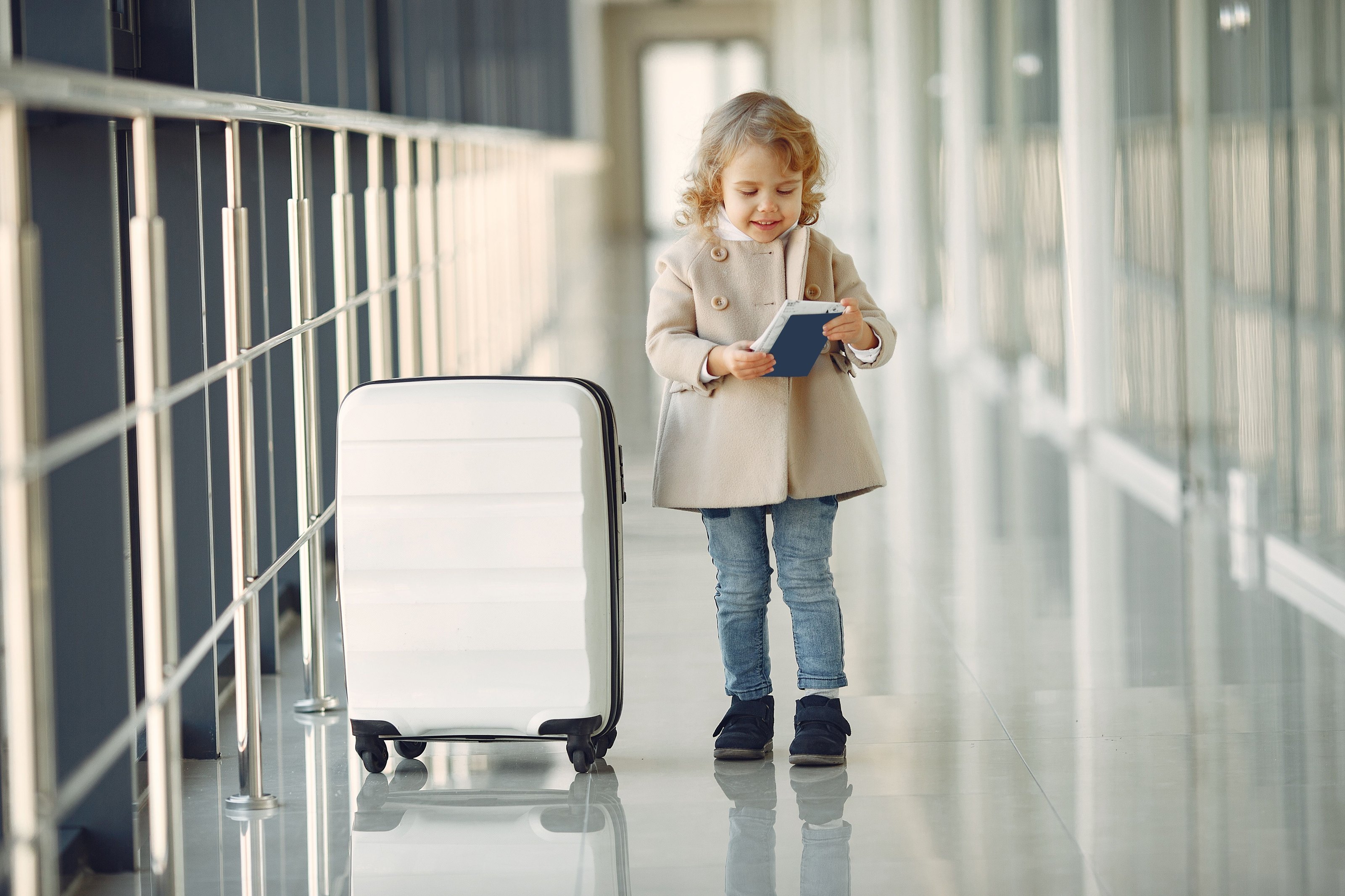 A little girl with a passport and a suitcase in an airport corridor