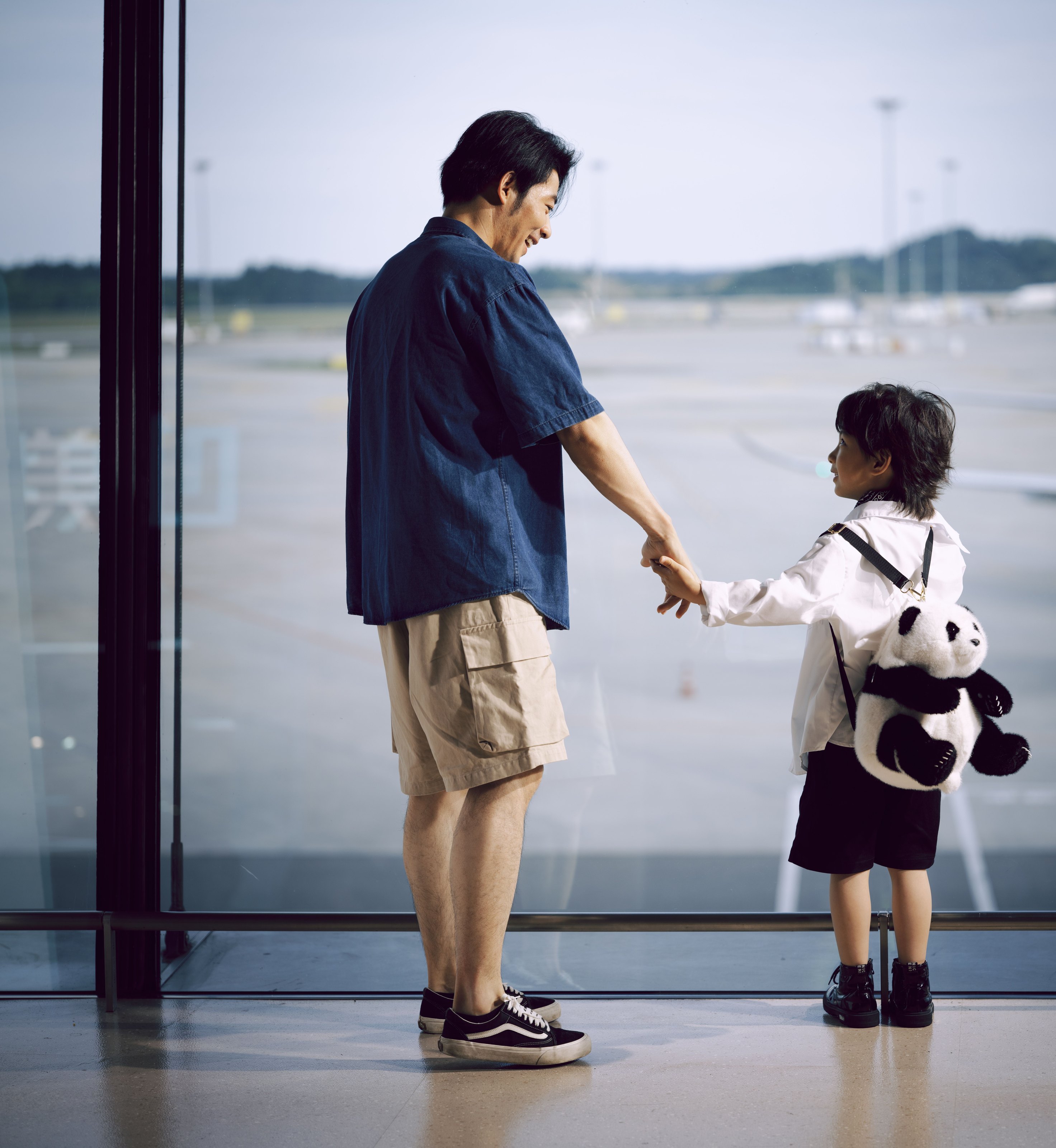 A man and a child holding hands at a large airport window